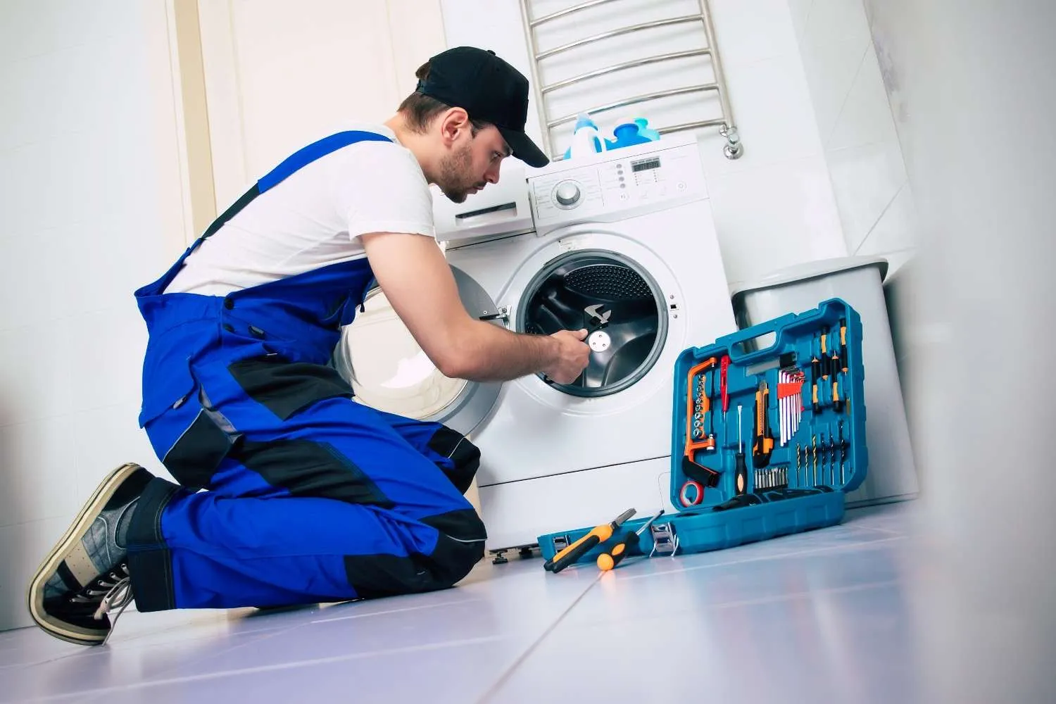 Technician kneeling beside a front load washing machine with an open tool case